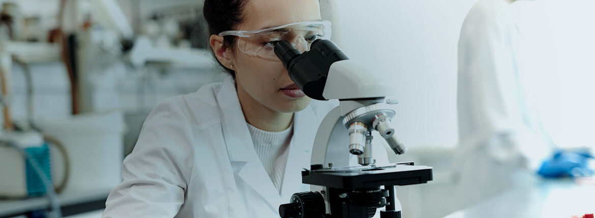Female lab technician looking through a microscope- Healthcare & Biotech